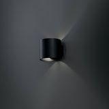 Rond black up and down wall light in a styled room, emphasizing its versatility and design appeal.