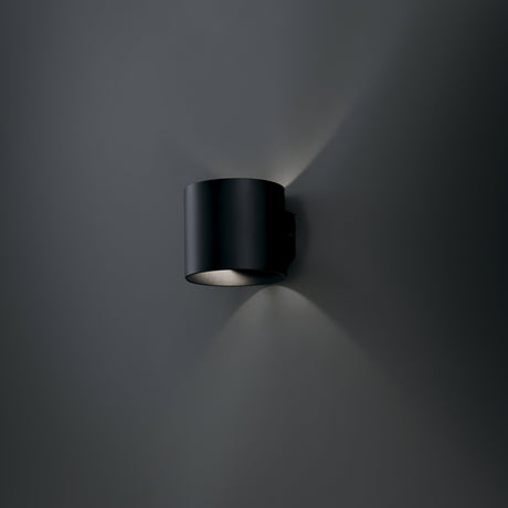 Rond black up and down wall light in a styled room, emphasizing its versatility and design appeal.