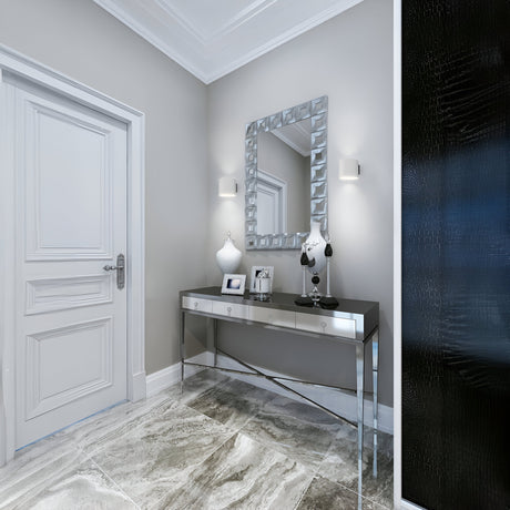 A modern hallway features a matte white door, stylish gray walls, and a glossy tiled floor. A mirrored console table with decorative items is beneath a geometric mirror. Illuminated by two Rond Up & Down Wall Lights in white, the space includes a textured black feature wall partially visible.