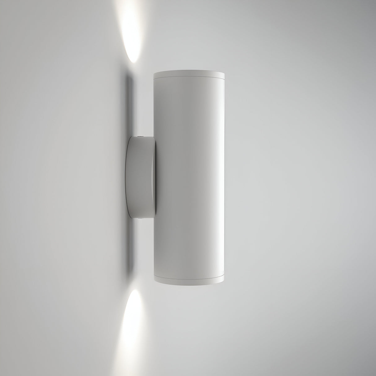 The FOCUS S Up & Down Wall Light - White, mounted on a white wall, features a modern cylindrical design and uses GU10 bulbs to emit light from both the top and bottom, creating elegant bright spots.