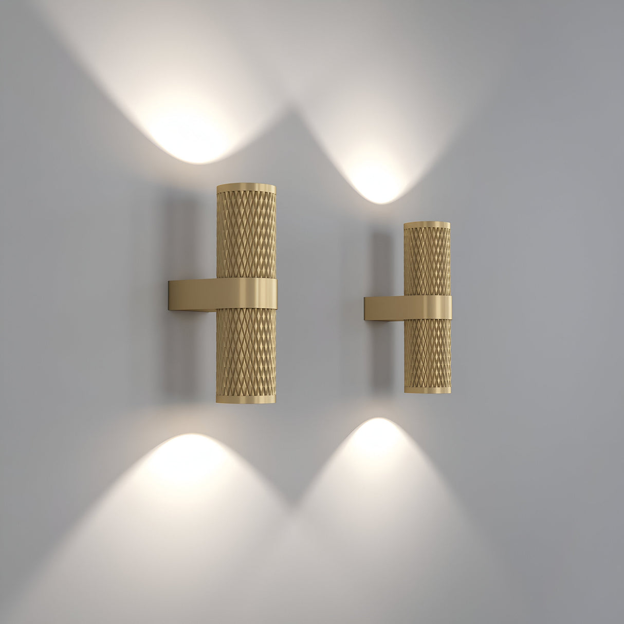 Two Focus Design Up & Down Wall Lights in matte gold are mounted on a light gray wall, featuring a cylindrical mesh design. They emit soft architectural illumination from the top and bottom, casting a gentle glow that enhances their contemporary aesthetic.