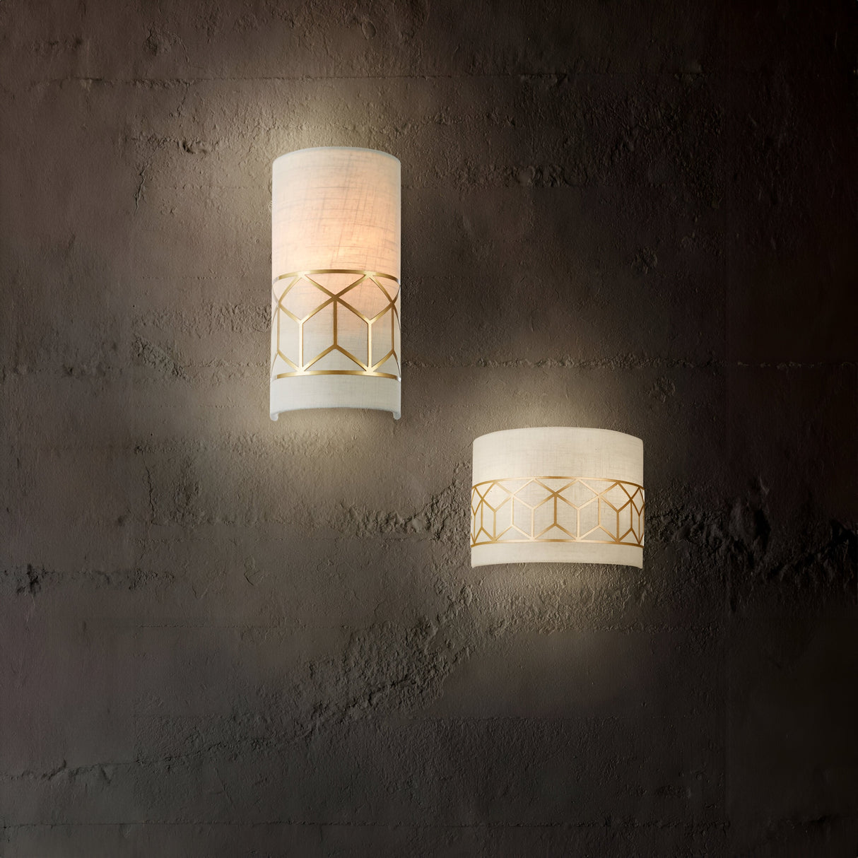 The Messina Wall Light in gold, with its linen shade, emits a warm glow on a textured dark wall. This ambient lighting highlights the intricate geometric designs, creating an elegant and cozy atmosphere.