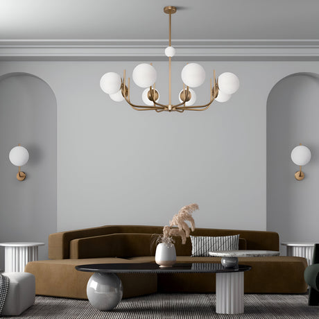 A modern living room showcasing a brown sectional and two small white side tables. A black coffee table holds a white vase with dried plants, while the Rendez-vous 8 Light Chandelier - Brass and matching wall sconces illuminate the space against light gray walls.