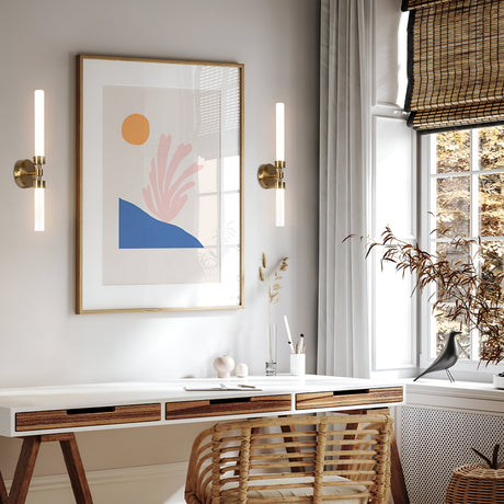 Bright, stylish home office featuring a white desk and wooden chair. A framed abstract art piece hangs on the wall between two Stelo 2 Light LED Wall Lights in brass. A large window with bamboo blinds and a potted plant enhance the cozy, natural ambiance.