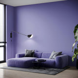 A modern living room has pastel purple walls and a matching sofa with gray cushions. The Mollis Adjustable Wall Light in sleek modern style pairs with an arc floor lamp featuring a black and white shade. A plant by the large windows lets natural light flood the space.