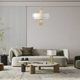 A modern living room exuding elegance with a green velvet sofa, round coffee table, and gold accents. The focal point is the Impressive 5 Light Chandelier - Gold adorned with gold-tone chains. Other features include a striped white wall panel, green plant, decorative objects, and a plush beige rug.