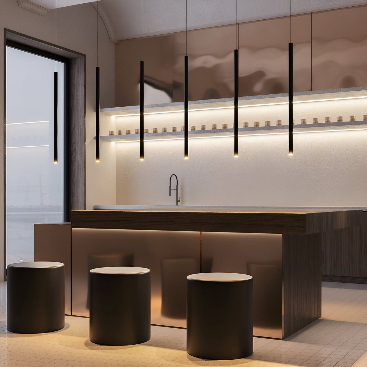 The modern kitchen features sleek dark cabinetry and a long island with five cylindrical stools. Above the island hang Pro Extra LED Long Thin Pendant Lights in white, enhancing the minimalist design. A large window on the left floods natural light into this stylish space.