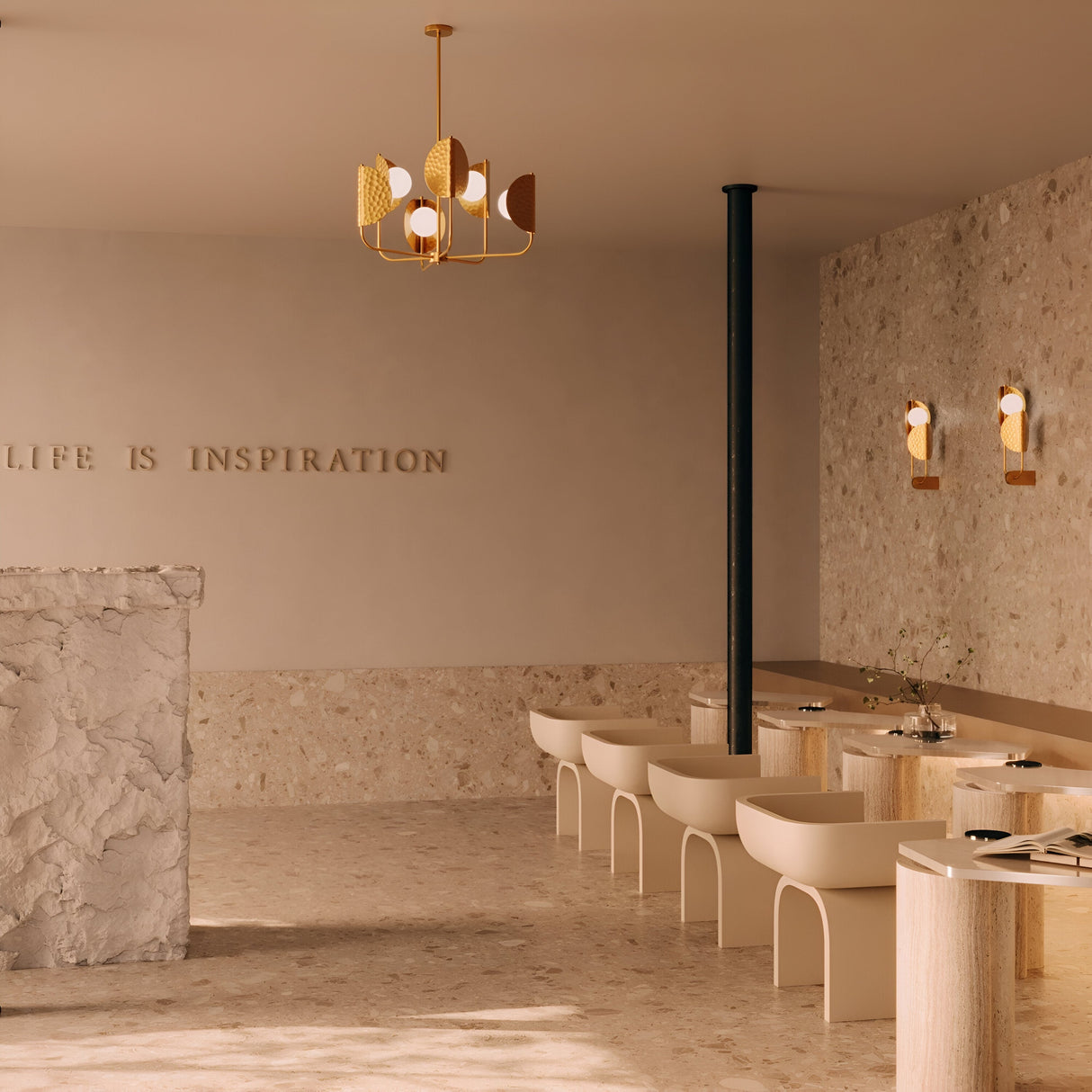 A minimalist cafe interior showcases a marble counter and cream-colored chairs and tables. Brass Tropic 2 Light Left High Wall Lights illuminate the space. A modern chandelier hangs overhead, while ethnic-inspired patterns accompany the wall phrase LIFE IS INSPIRATION.