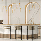 The cafes modern interior features a sleek white marble counter with light wood accents, lined by three high chairs. Elegant Imaginary Chain Pendant Lights in gold hang from the ceiling, while large arched marble wall features are softly backlit.