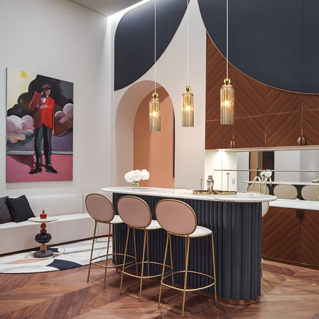 A modern interior with a stylish kitchen island, three tall chairs, and vintage charm from the Antic Pendant Light - Gold With Cognac Ribbed Glass. Geometric patterns and wood accents enhance the decor. A colorful painting near a cushioned bench adds warmth to the space.