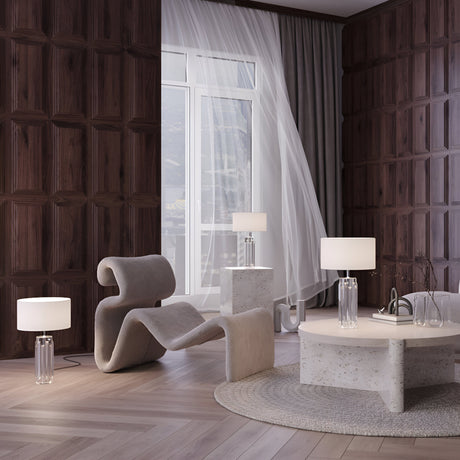 In a modern living room, a wavy chair, round rug, and a chrome-based coffee table in neutral tones complement the decor. Three Muse Table Lamps - Chrome With White Shade illuminate the space. Sheer curtains hang by the tall windows, and dark wood paneling enhances its contemporary feel.