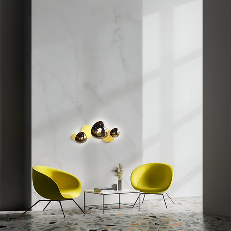 A minimalist room showcases two yellow chairs facing a small table on a terrazzo floor. Mounted on the large white wall, a cluster of Jack-stone LED Wall Lights 13W 3000K Gold casts shadows. Sunlight patterns enhance the contemporary design through a window.