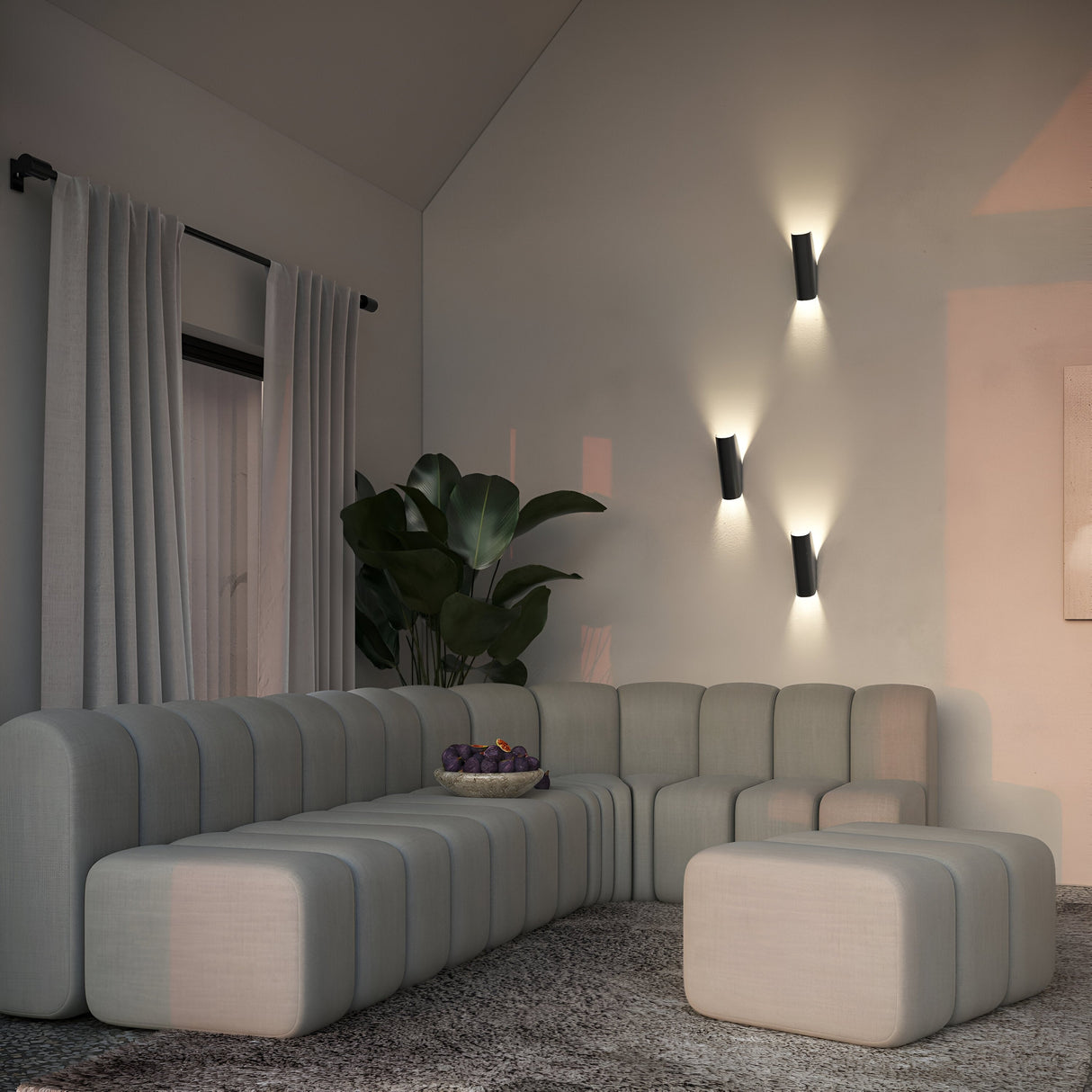 A modern living room showcases a modular gray sofa with an ottoman on a textured rug. Three black Notta Bidirectional Wall Lights provide a cozy ambiance, complemented by a potted plant near the windows flowing curtains. A bowl rests invitingly on the sofa.