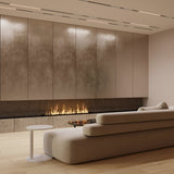 A modern living room boasts a minimalist design with a sleek LED linear fireplace in a textured wall. A large beige sectional sofa faces the fire, while light hardwood floors and discreet Points LED Linear Track Lights for Magnetic Exility create ambiance. A small round table completes the cozy setup.