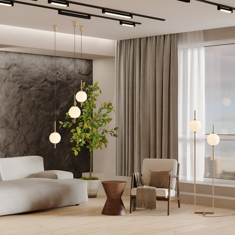 A modern living room features a light gray sectional sofa, wooden side table, and two chairs. A potted plant is beside a textured dark wall. The Sixth Sense LED Pendant Light in white glass and brass brings warmth. Floor-length curtains on a large window offer an outdoor view.