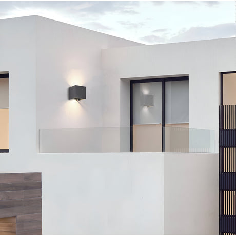The modern white building with geometric lines showcases a glass balcony and two Fulton Outdoor LED Rectangular Wall Lights in black. Its architecture has large windows with dark frames, and the cloudy sky highlights corrosion-resistant aluminum paneling on the left.