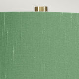 The Isla 1 Light Table Light - White/Green is captured in a close-up that highlights its textured green shade accented with subtle vertical stripes and topped with a small brass finial. Placed against a neutral backdrop, this lamp pairs elegantly with its white ceramic base, blending sophistication with an understated design.