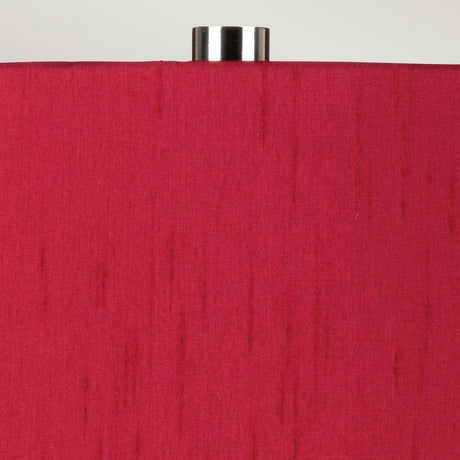 Close-up of the Isla 1 Light Table Light, showcasing a red fabric shade embellished with vertical thread patterns. Its white ceramic base harmonizes beautifully with the vibrant shade, and it is elegantly topped with a silver metal finial, all against a simple light gray background.