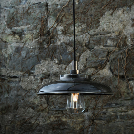 Islura Brass Pendant Light IP65 with a wide, shallow dark metal shade and glass cover enclosing an E27 bulb, shown against a stone wall background.