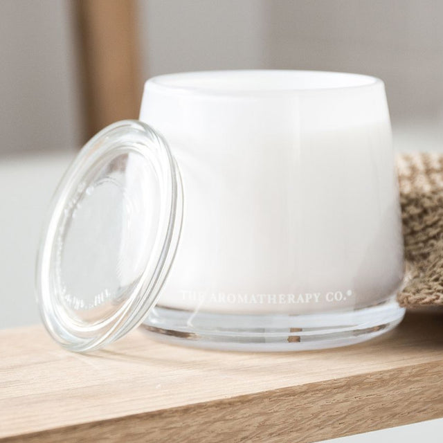 Uplift Sweet Lime & Mandarin scented candle, 260g, in a rounded white jar with clear glass base and lid resting open beside it on a wooden shelf.