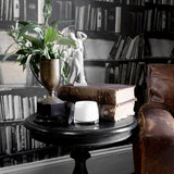 Uplift Sweet Lime & Mandarin scented candle in a white jar with clear lid, displayed on a dark side table beside books, a trophy vase, and a statuette.