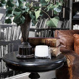 Uplift Sweet Lime & Mandarin Scented Candle 260g in a white jar with clear lid, displayed on a black side table beside vintage books and a leafy plant.