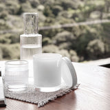 Neroli & Amber Wood Scented Candle 400g in a round white vessel with lid, styled on a woven mat beside ribbed glass tumblers on a wooden table.