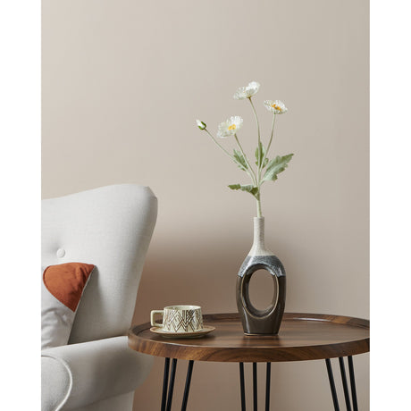 Iwate ceramic vase with narrow beige speckled neck and glossy black open-oval base, styled with a daisy stem on a wooden side table beside a light armchair.