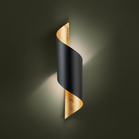 Jabaloyas Wall Light in matt black steel, curled into a spiral with a gold leaf interior that glows softly, mounted on a dark green wall.