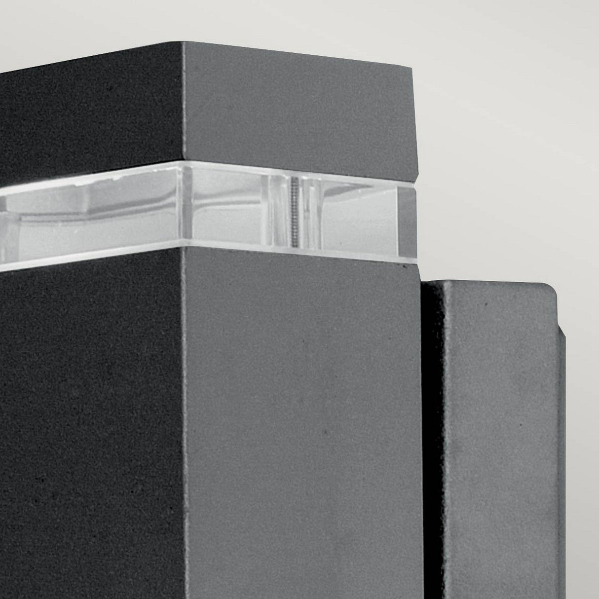 Close-up of a sleek, minimalist building facade adorned with dark, rectangular panels and a translucent strip. The design showcases clean lines and geometric shapes, enhanced by the modern style of the Jannik 2 Light Outdoor LED Wall Light in Graphite, which highlights the structure’s energy efficiency.