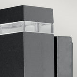 Close-up of a sleek, minimalist building facade adorned with dark, rectangular panels and a translucent strip. The design showcases clean lines and geometric shapes, enhanced by the modern style of the Jannik 2 Light Outdoor LED Wall Light in Graphite, which highlights the structure’s energy efficiency.