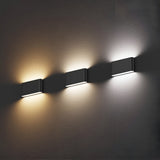 Three Jens-1 LED Outdoor Wall Lights in black are mounted on a textured surface. Each IP65-rated light emits a different color: warm yellow on the left, soft white in the middle, and cool white on the right, casting subtle shadows below them.