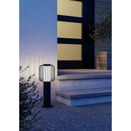 Jerbine Bollard Light in black, lit beside outdoor steps at night, with a slim post and lantern-style cage head glowing white, IP54 rated for garden use.