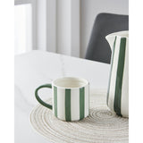 Jinjiti Mug in white ceramic with bold green vertical stripes and a green handle, shown beside a matching striped jug on a marble table.
