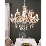 Joressa Glass 18 Light Pendant in chrome, a two-tier chandelier with twisted cognac glass arms, candle bulbs and faceted glass droplets, shown above a dining table.