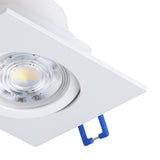 Close-up of the Kamarne LED Downlight in white, showing the square aluminium frame, round lens with warm white light, and blue adjustable mounting clips, on a plain background.