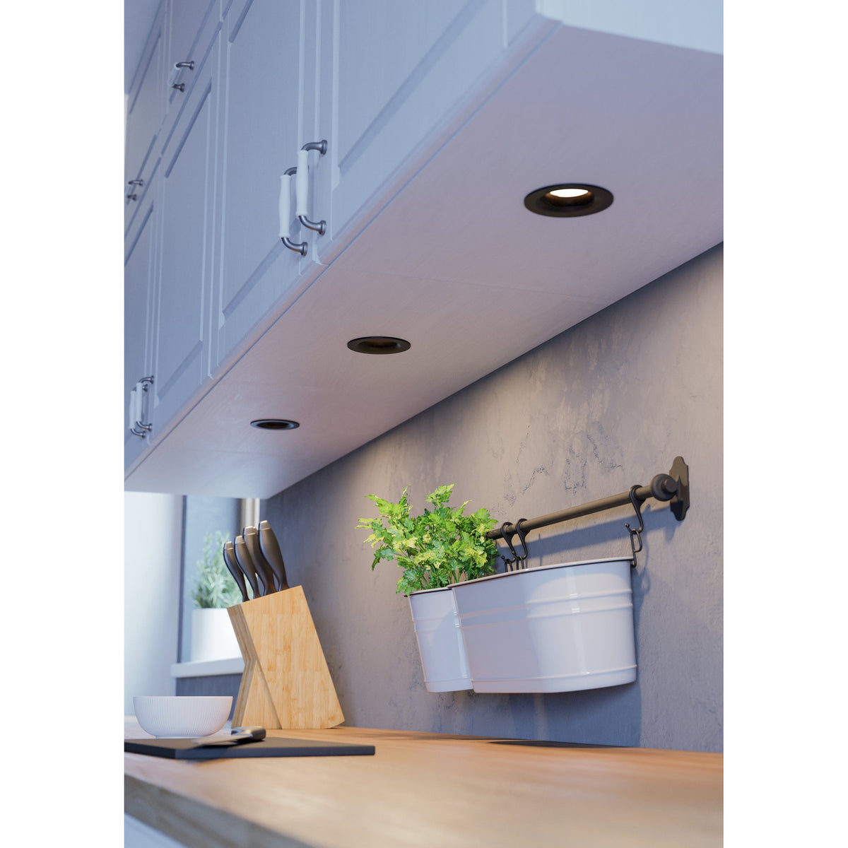 Kamarne LED Downlight set of 3 in black with aluminium body, recessed under white kitchen cabinets above a wooden countertop.