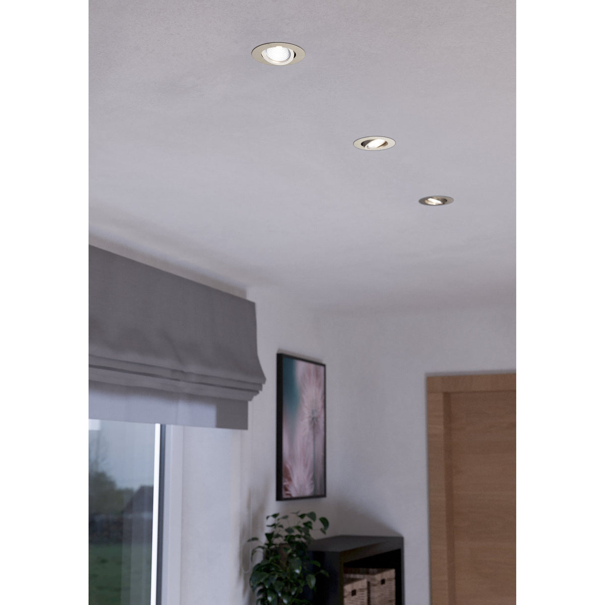 Three round Kamarne LED downlights with satin nickel trims recessed into a white ceiling, shown lit in a room with a window blind and wooden door.