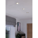 Three round Kamarne LED downlights with satin nickel trims recessed into a white ceiling, shown lit in a room with a window blind and wooden door.