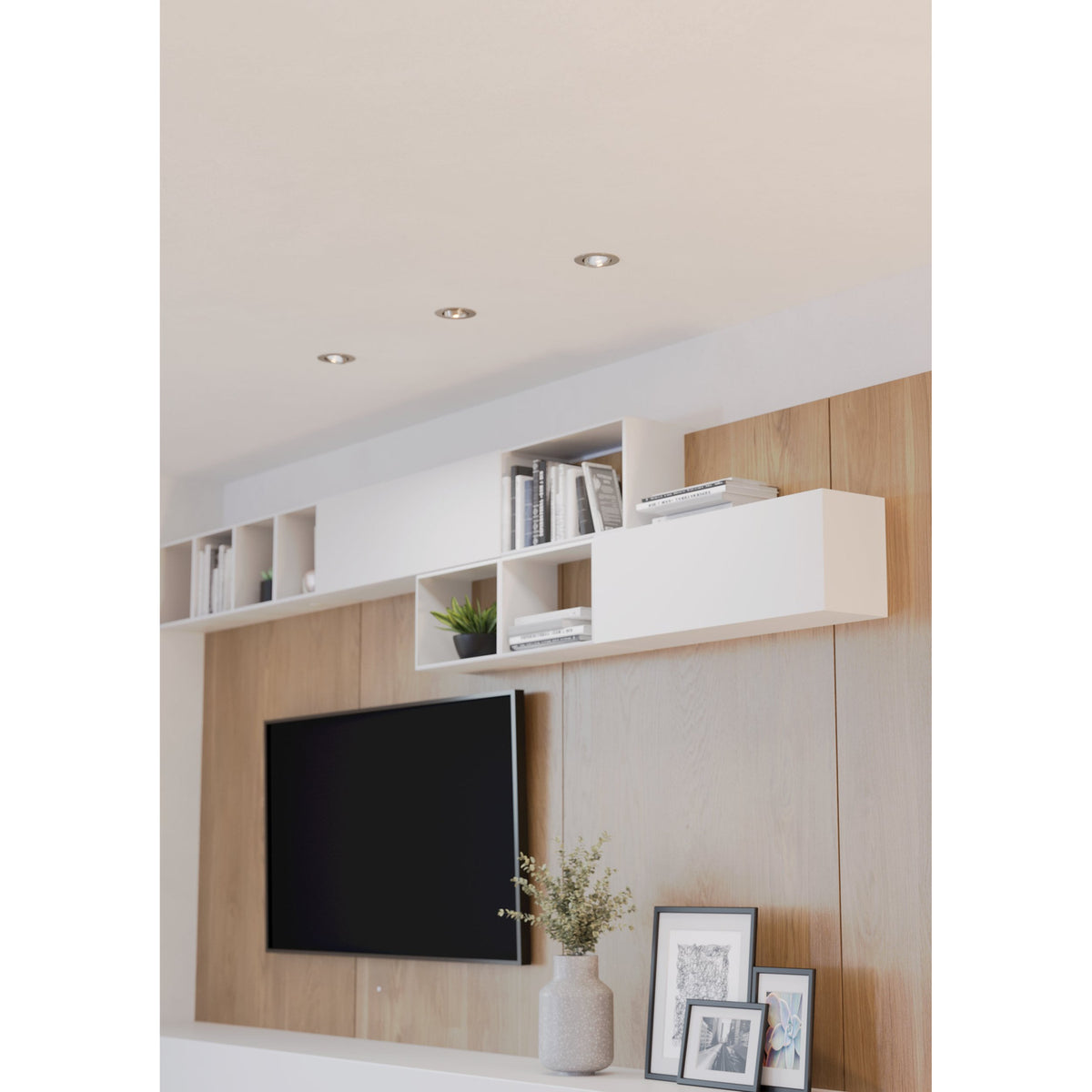Kamarne LED downlights recessed into a living room ceiling with satin nickel trims, shown above a wood-panelled wall with shelving and a mounted TV.