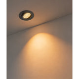 Kamarne black round recessed LED downlight in a ceiling, tilted head casting warm light down a light grey wall.