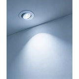 Round white recessed LED downlight from the Kamarne set installed in a ceiling, tilted centre casting a bright beam onto a plain grey wall.
