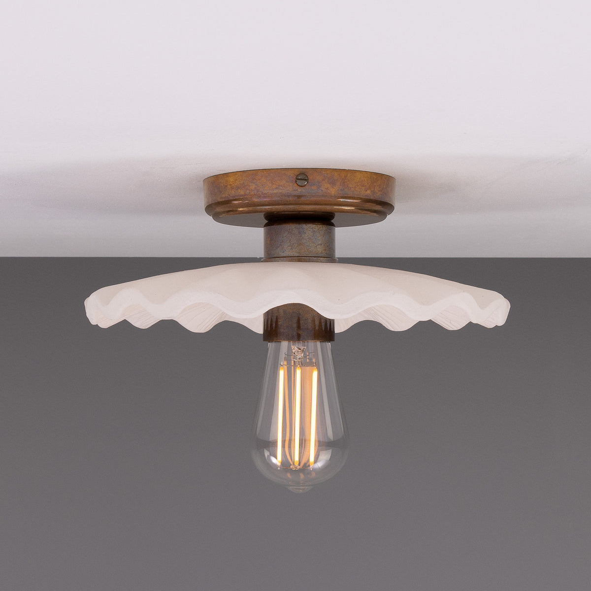 Kapok ceramic ceiling light with a scalloped matt white striped shade, aged brass ceiling plate and lampholder, shown with an exposed bulb against a plain background.