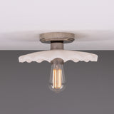 Kapok ceramic ceiling light with a scalloped, matt white striped shade and aged metal lampholder, shown lit with a vintage filament bulb against a grey background.