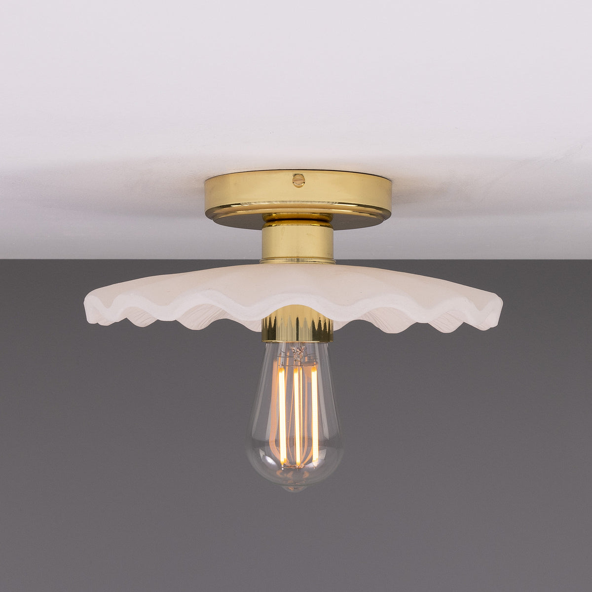 Kapok ceramic ceiling light with a wide scalloped matt white striped shade, brass lampholder and round ceiling plate, shown with an exposed bulb against a plain background.