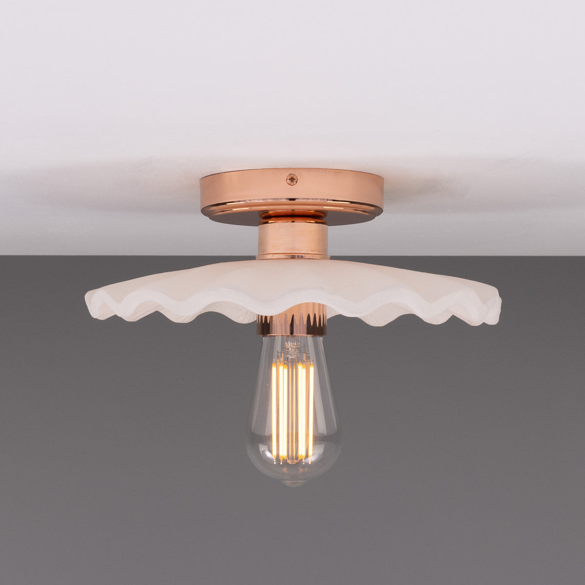 Kapok ceramic ceiling light with a scalloped, ribbed matt white shade, copper lampholder and ceiling plate, and exposed filament bulb, shown against a plain grey background.
