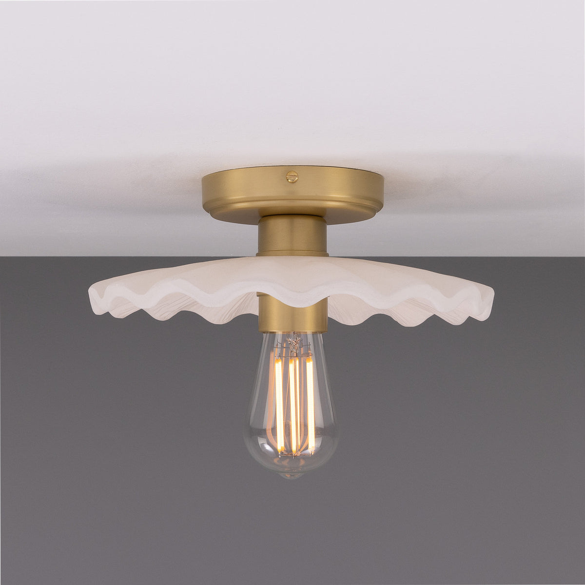 Kapok ceramic ceiling light with a wide scalloped shade in matt white striped glaze, brass lampholder and ceiling plate, exposed bulb, shown against a plain grey background.