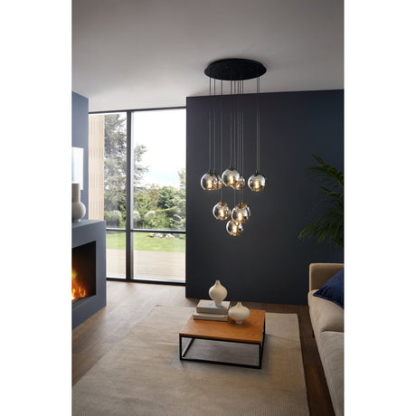 Karnarne Smoked Glass 10 Light Pendant in black, staggered globes on black cables from a round ceiling canopy, shown above a coffee table in a living room with dark wall.