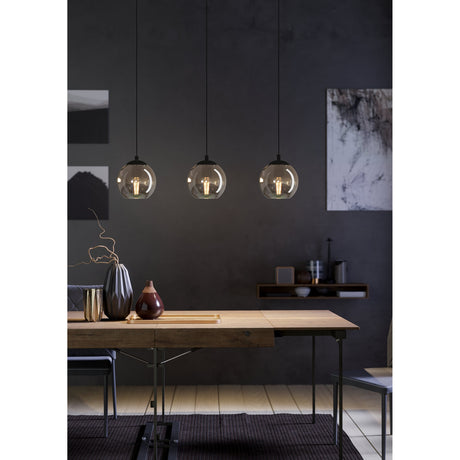Karnarne Smoked Glass Linear Pendant Light in black, three round globe shades on black cords, shown above a wooden dining table in a dark-walled room.