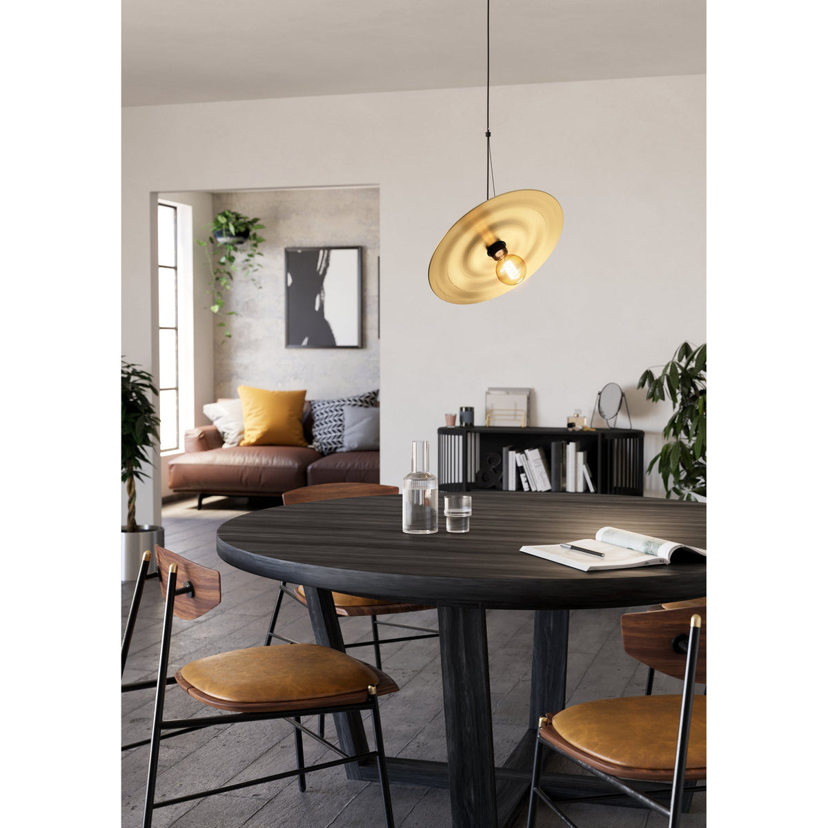 Karnette Pendant Light with black cord and canopy, featuring a wide, shallow brushed brass disc shade, hung above a round dark wood dining table.